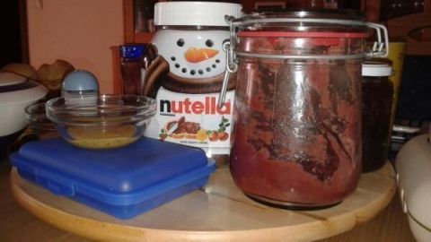 Ein Drehteller auf einem Esstisch trägt ein Nutella-Glas, ein Einweckglas mit Marmelade und blauen Behälter.