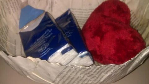 Eine Schale aus Buchseiten hält ein rotes Herz und zwei Packungen Taschentücher, dekorativ arrangiert auf einem Tisch.