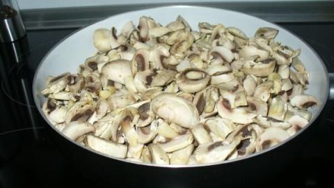 In einer großen Pfanne liegen gebratene Champignons, die auf dem Herd vorbereitet werden, um sie platzsparend einzufrieren.
