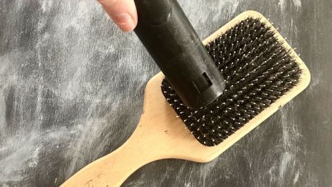 Die Haarbürste wird mit einem Staubsauger gereinigt, um Haare zu entfernen, auf einer hellen, glatten Oberfläche.