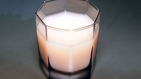 Ein Glas mit milchiger Flüssigkeit steht auf einer glatten Oberfläche, umgeben von einem neutralen Hintergrund.