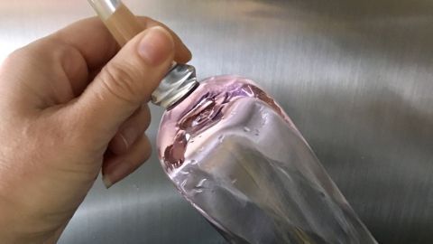 Ein schmaler Sektglas wird mit einer Hand abgetrocknet, während es über eine glänzende, metallische Oberfläche gehalten wird.