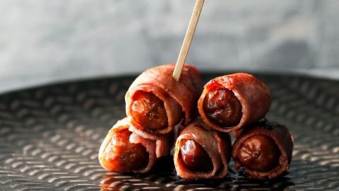 Saftige Datteln sind in Serrano-Schinken gewickelt und auf einem eleganten, dunklen Teller angerichtet.