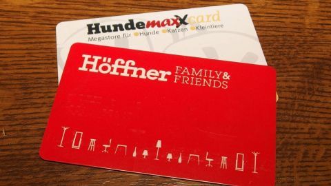 Zwei Kundenkarten liegen auf einer Holzoberfläche. Die rote Karte gehört zu Höfner und die weiße zu Hundemaxx.