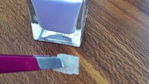 Ein Nagellackfläschchen steht auf einem Tisch, während ein Pinsel den Eingerissenen Fingernagel sorgfältig behandelt.