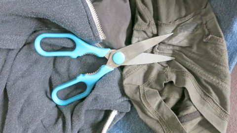 Zwei Scheren liegen auf einem Haufen Kleidung, während hartnäckige Flecken auf den Stoffen sichtbar sind.