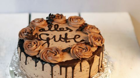 Eine dekorierte Torte mit Rosendekoration aus Schokolade und der Aufschrift "Alles Gute" auf einer silbernen Unterlage.