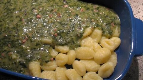 Gnocchi mit Spinat und Schinken liegen in einer blauen Auflaufform, überbacken und goldbraun gebräunt.