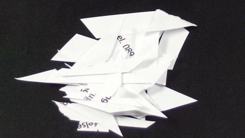Zerknitterte, unsortierte Papierschnipsel liegen auf einem schwarzen Untergrund, was auf unsachgemäße Briefentsorgung hindeutet.