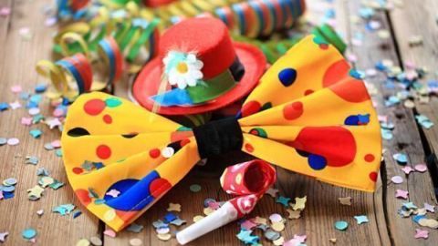 Eine bunte Krawatte liegt auf einem Holztisch, umgeben von Konfetti und kreisförmigen Luftschlangen, passend zum Karneval.