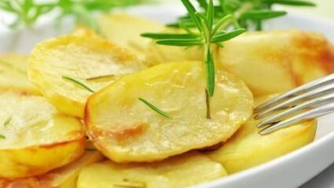 Goldbraune, knusprige Bratkartoffeln liegen auf einem weißen Teller, garniert mit frischen Kräutern und einer Gabel daneben.