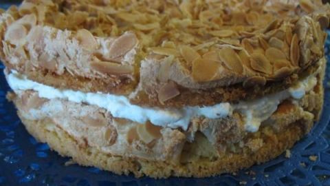 Eine Sahnetorte mit knusprigem Mandelbelag liegt ausgestellt auf einer blauen Tortenspitze.