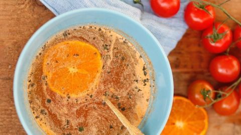 Eine Schüssel Orangen-Tomaten-Suppe mit einer Orangenscheibe und einem Löffel, umgeben von frischen Tomaten.