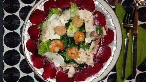 Ein Salat aus roten Beeten, Garnelen und Pilzen liegt auf einem Teller. Daneben sind eine Gabel, ein Messer und eine Serviette.
