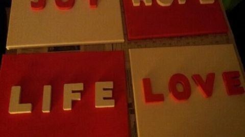 Bunte Leinwände zeigen Worte wie "JOY", "HOPE", "LIFE" und "LOVE" auf weißem und rotem Hintergrund in kreativer Wanddeko.