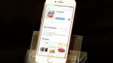 Smartphone steht in einer umfunktionierten Kassettenhülle aufrecht, zeigt App namens "Frag Mutti" auf schwarzem Hintergrund.