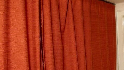 Ein roter Flächenvorhang hängt in einem Raum und bedeckt ein Fenster, um Licht zu dämpfen und Privatsphäre zu bieten.