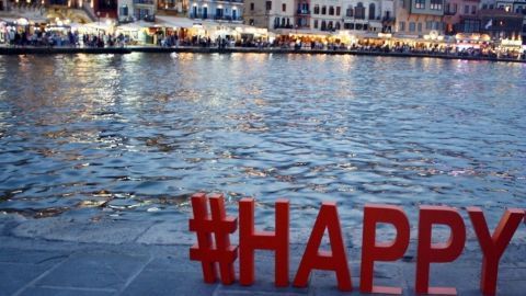 Rote Buchstaben mit der Aufschrift #HAPPY stehen am Ufer eines ruhigen Wassers während des Abenddämmerungslichts.
