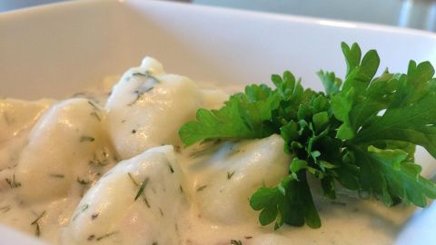 Saure Rahmkartoffeln liegen in einem weißen Schälchen, umgeben von einer cremigen Soße und frischem Grün.