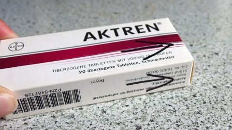 Eine Hand hält eine Medikamentenpackung mit der Aufschrift "AKTRENE", während Pfeile die Öffnung anzeigen.