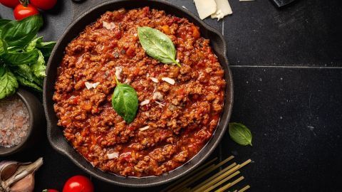 Eine Pfanne mit würzigem Hackfleisch und Zigeunersoße, umgeben von frischen Zutaten wie Basilikum und Tomaten.