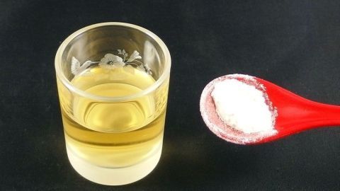 Ein Glas mit goldenem Flüssigkeit steht neben einem roten Löffel mit weißem Pulver, das zur Linderung von Zahnschmerzen verwendet werden kann.