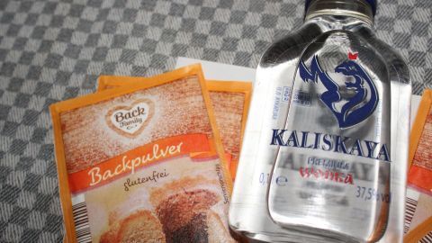 Backpulver und eine Flasche Kaliskiya stehen auf einem karierten Tisch, um den Einsatz von Alkohol als Backpulverersatz zu zeigen.