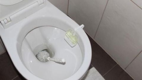 WC-Bürste reinigt Toilettenschüssel, daneben ein Lufterfrischer, in einem gefliesten Badezimmer.