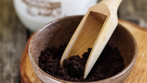 Eine Schale mit löslichem Kaffeepulver steht neben einem Glas mit Kokosnussöl auf einem Holzbrett.