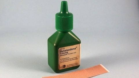 Eine grüne Flasche mit einem punktierten Verschluss steht neben einem hautfarbenen Pflaster, das für die Behandlung von Dornwarzen verwendet wird.