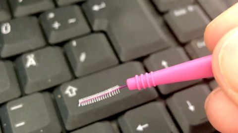 Eine Hand hält ein pinkes Reinigungswerkzeug über die Tastatur, um den Zwischenraum der Tasten gründlich zu reinigen.