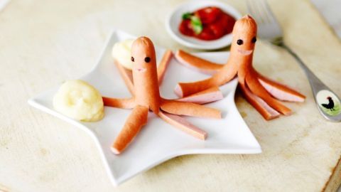 Zwei Würstchen-Tiere in Form von Tintenfischen sitzen auf einem Teller, begleitet von Kartoffelbrei und Ketchup.