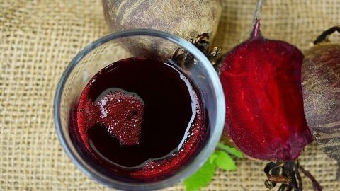 Ein Glas mit künstlichem Blut aus Rote Bete steht auf einem Jutestoff, umgeben von frischen Rüben für Karneval.