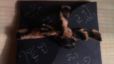 Schwarze Geschenkkarte mit aufgedrucktem "Für Dich", dekoriert mit einem braun-schwarzen Band, liegt auf einem Holztisch.