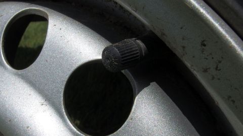 Eine Ventilkappe am Reifen wird gelöst, um den Luftdruck im Auto zu überprüfen, umgeben von einer Felge.