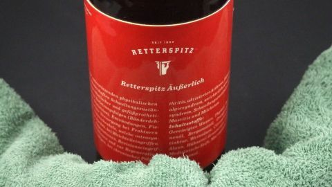 Ein Rotweinflasche mit dem Etikett „Retterspitz“ wird von zwei grünen Tüchern gehalten, um Halsschmerzen zu lindern.