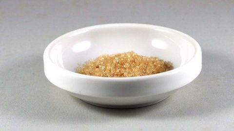 Brauner Zucker liegt in einer weißen Schüssel. Der Zucker befindet sich in einem neutralen, hellen Umfeld.