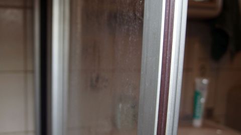 Eine Duschwand mit hartnäckigen Kalkflecken steht im Fokus, umgeben von einem Badezimmer mit weiteren Hygieneprodukten.