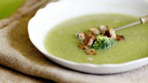 Brokkoli-Apfelcremesuppe in weißem Teller auf grobem Stoff, garniert mit Croutons und Brokkoli.