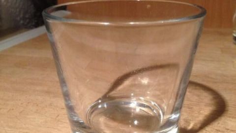 Ein leeres Glas steht still auf einer Holzarbeitsfläche in einer Küche. Keine Wachsreste erkennbar.