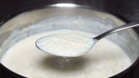 Ein Löffel mit Milchreis ist in eine Schüssel getaucht, während er im Topf auf dem Herd köchelt. Energiesparen beim Kochen!