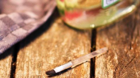 Ein kleiner Spatel liegt auf einem Holztisch neben einer Flasche Flüssigkeit, bereit zur Anwendung gegen Nagelpilz.
