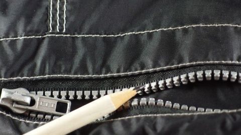 Ein Bleistift wird verwendet, um einen klemmt Reißverschluss auf einer schwarzen Jacke zu lösen und zu reparieren.