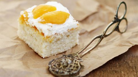 Ein Stück Aprikosen-Vanille-Blechkuchen liegt auf braunem Papier, neben einem antiken Kuchenteil.