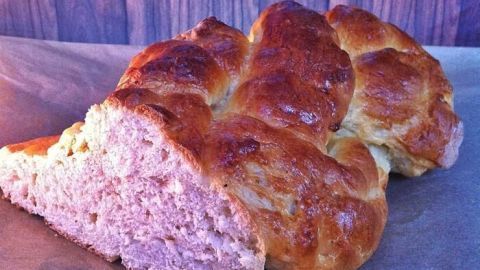 Ein goldbrauner Brioche Striezel liegt auf Backpapier, im Hintergrund eine Holzverkleidung.