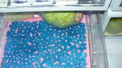 In einem Kühlschrank liegt eine blaue Spülbeckeneinlage auf einer Ablage, um frisches Gemüse aufzubewahren.