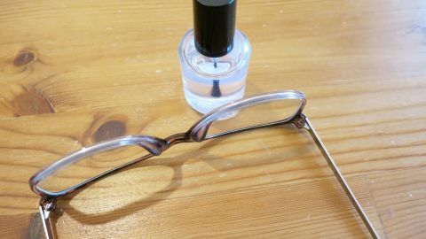 Ist eine Schraube an der Brille locker? Ein Tropfen farbloser Nagellack lässt sie für immer festsitzen. Eine Brille liegt auf einem Holztisch neben einem Fläschchen Nagellack, bereit zur Reparatur einer lockeren Schraube.