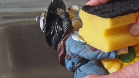 Zahnpasta zum Polieren von Keramik oder Metall verwenden. Eine Figur hält einen Schwamm über einem Waschbecken, während sie gründlich mit der Zahnpasta den Schwamm reinigt.
