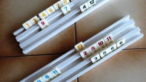 Spielsteine liegen auf zwei weißen Halterungen mit Zahlen in verschiedenen Farben auf einer braunen Fliesenoberfläche.
