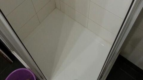 Eine saubere Dusche mit einem Abfluss in der Mitte und einem Eimer nebenan, bereit für die Dusche reinigen.